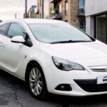 A white Vauxhall Astra GTC parked on a city street next to a modern building.
