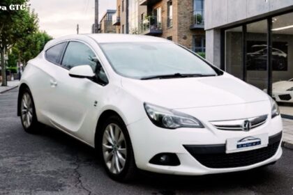 A white Vauxhall Astra GTC parked on a city street next to a modern building.
