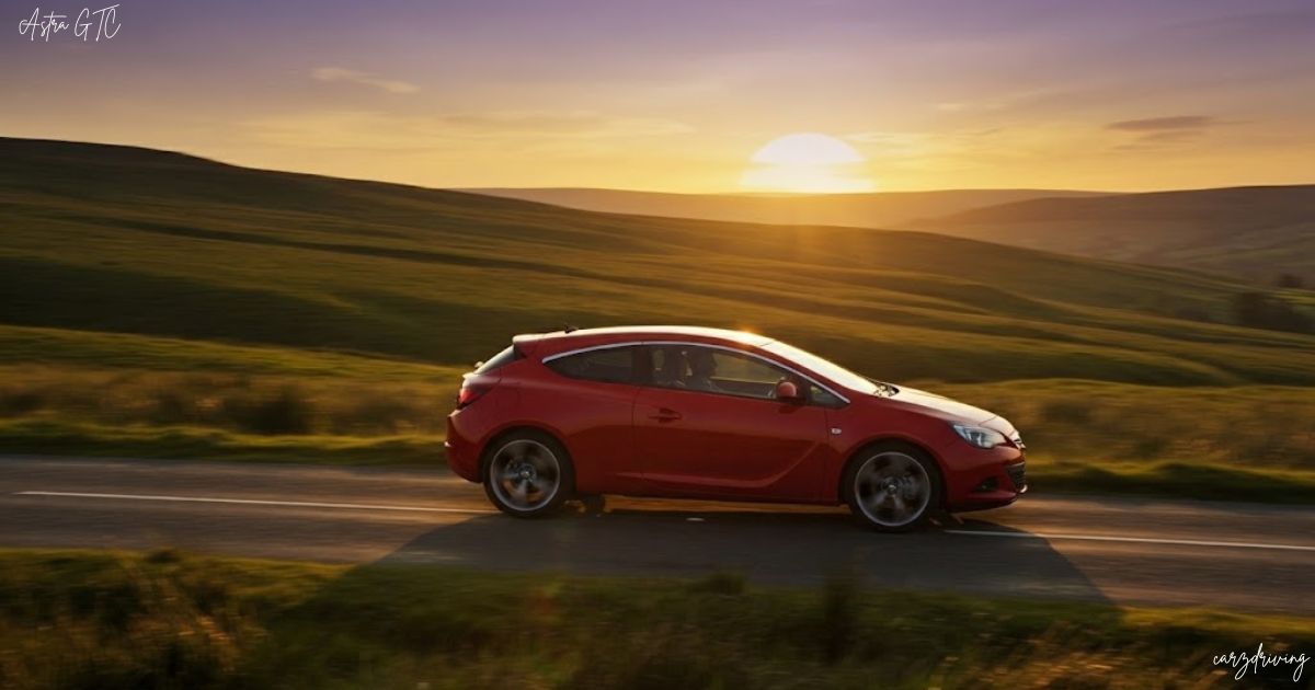 A red Opel/Vauxhall Astra GTC coupe driving on a winding country road during a golden sunset, with rolling green hills in the background.