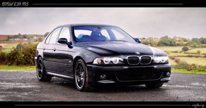 Front-three-quarter view of a dark metallic BMW E39 M5 sedan with iconic halo headlights parked outdoors.