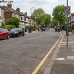 A residential street lined with terraced brick houses, featuring a single yellow line painted along the curb on the right side and a traffic sign that reads "No Waiting Mon-Sat 8am-6pm".at the corner lay can you park on a single yellow line