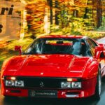 A classic red Ferrari 288 GTO moving fast along a tree-lined asphalt road during peak fall foliage