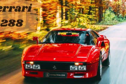 A classic red Ferrari 288 GTO moving fast along a tree-lined asphalt road during peak fall foliage