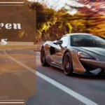 A grey McLaren 570S sports car driving along a scenic mountain road at sunset.