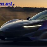 Front three-quarter dynamic shot of a deep purple McLaren W1 super sports car driving fast on a country road at dusk with headlamps illuminated.