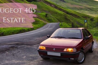 A dark red Peugeot 405 parked on the side of a paved mountain road surrounded by lush green hills. The car's headlights are illuminated, and a purple brushstroke graphic overlay in the top left corner displays the text "PEUGEOT 405 ESTATE" in white.