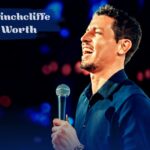 Comedian Tony Hinchcliffe smiling and holding a microphone on stage, with "Tony Hinchcliffe Net Worth" in bold white text overhead.