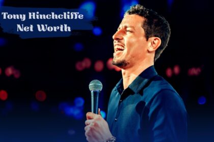 Comedian Tony Hinchcliffe smiling and holding a microphone on stage, with "Tony Hinchcliffe Net Worth" in bold white text overhead.