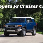 A blue and white Toyota FJ Cruiser car parked on a scenic, tree-lined paved road.