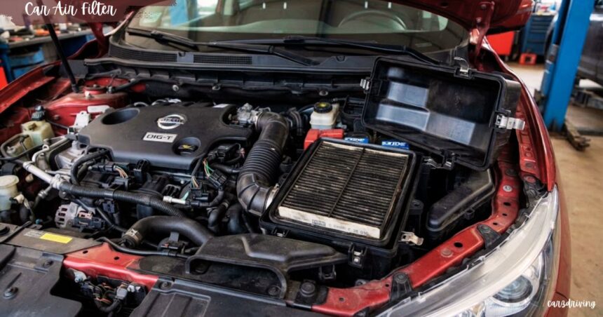 A dirty car air filter exposed inside its open black housing within the engine bay of a red car.