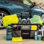 Complete car cleaning kit bag showing Detailmaster Pro car care products, spray bottles, applicator pads, and cleaning cloths set in front of a blue SUV.