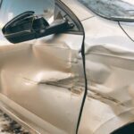 Close-up of a silver car showing severe structural and panel damage to the side doors and wing mirror, illustrating a Category S (Cat S) insurance write-off. explaining cat s car meaning