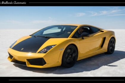 A yellow Lamborghini Gallardo Automatic sports car with a black hood driving across a vast open salt flat under a clear blue sky.