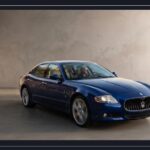 Blue Maserati Quattroporte V luxury sedan parked inside a modern studio showroom with neutral concrete textured walls and smooth flooring