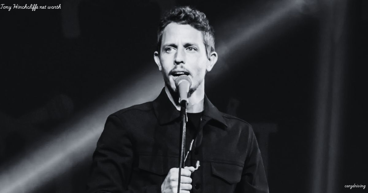 Black-and-white image of comedian Tony Hinchcliffe holding a microphone on stage, with the text "Tony Hinchcliffe net worth" in the upper-left corner.