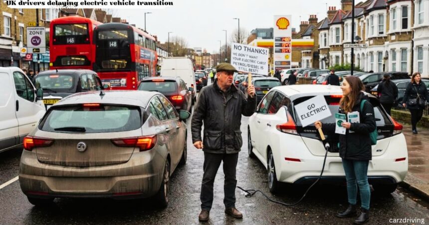 A UK driver holding a protest sign against switching to electric vehicles next to an EV charger at the corner lay uk drivers delaying electric car vehicle