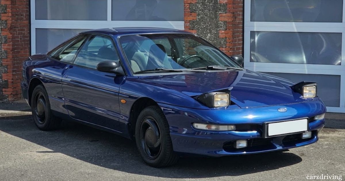 Dark blue Ford Probe automatic sports coupe parked outside a garage with pop-up headlights raised.