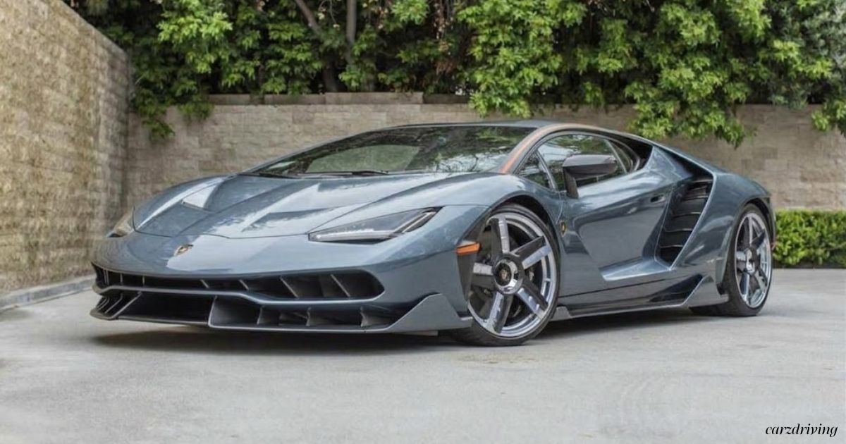 Grey Lamborghini Centenario Coupe parked on a paved driveway with stone wall background.